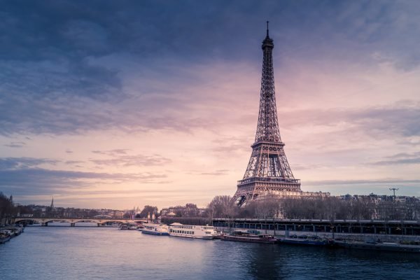 A beautiful wide shot of Eiffel Tower in Paris surrounded by water with ships under the colorful sky